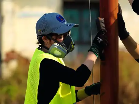 Voluntaria lijando un poste metálico antes de instalar la luminaria solar